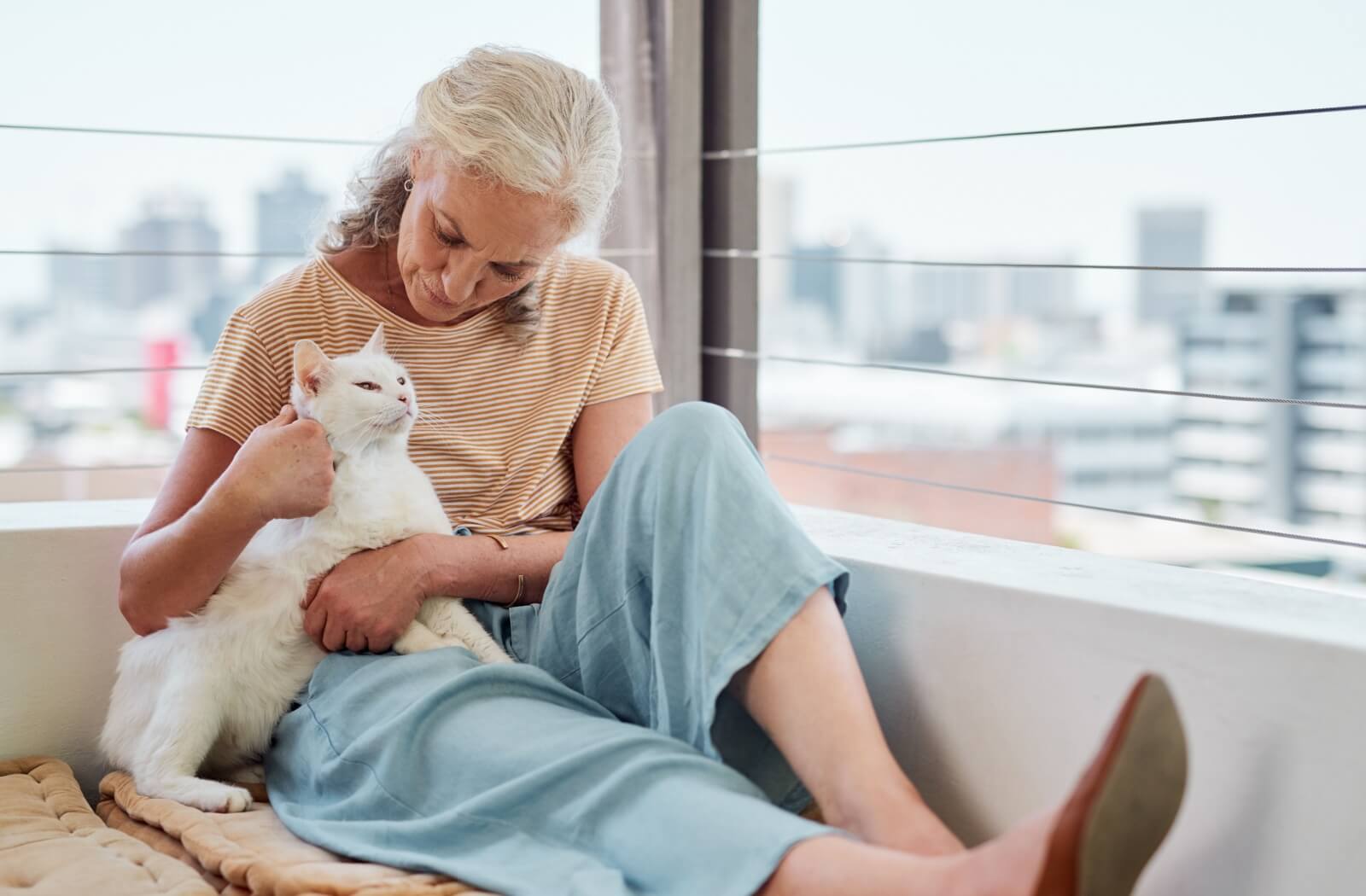 An older adult woman holding a white cat at home.