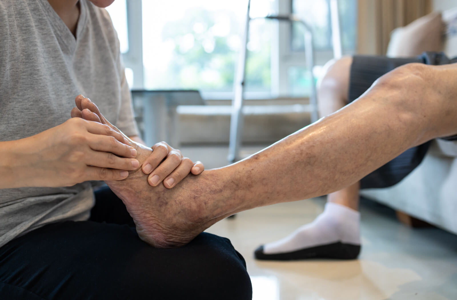 A physiotherapist rubbing an older adults foot and ankles to reduce the risk of swelling and discomfort.