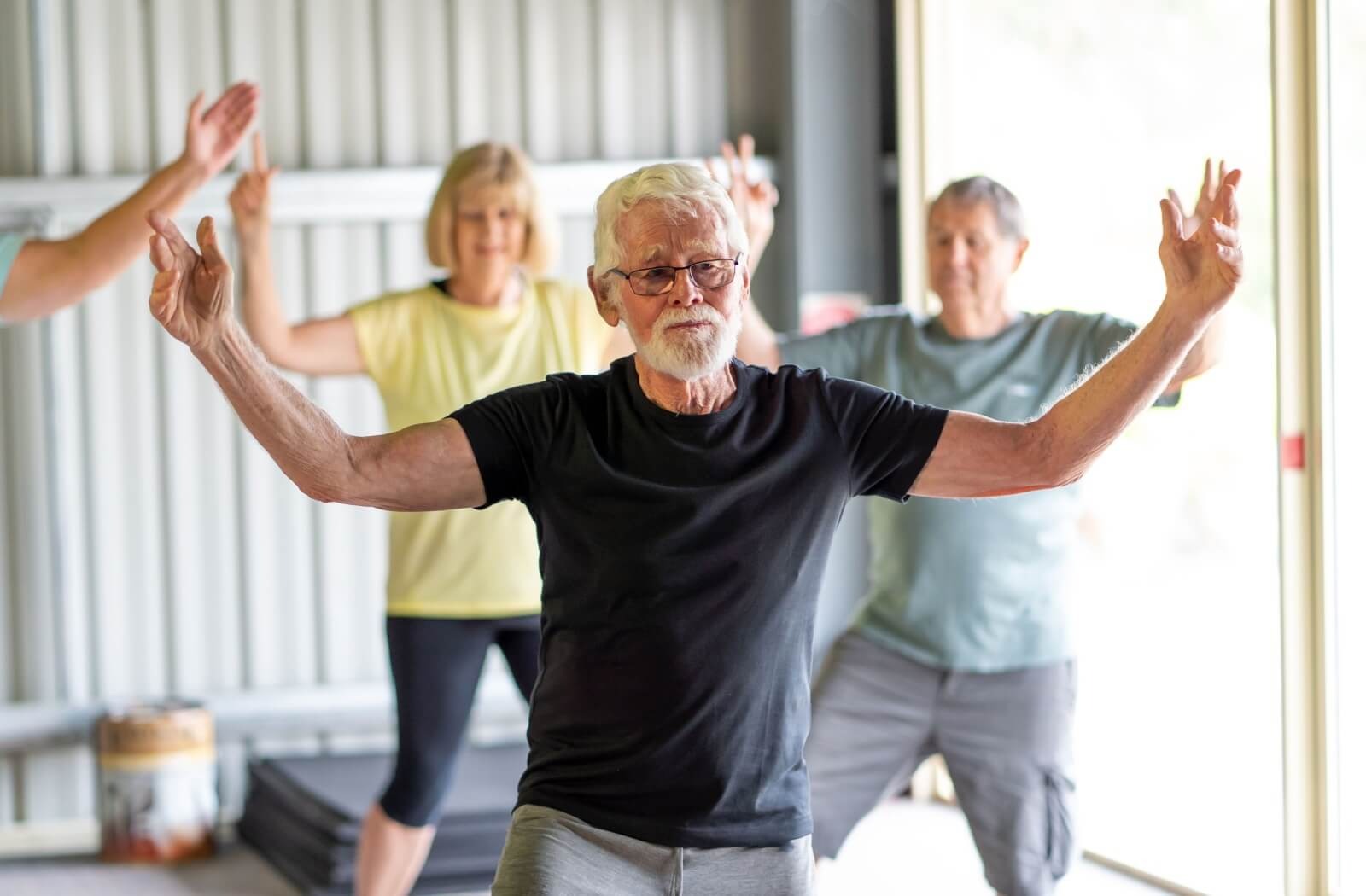 An older adult stretches their arms to either side while joining a group tai chi class in senior living