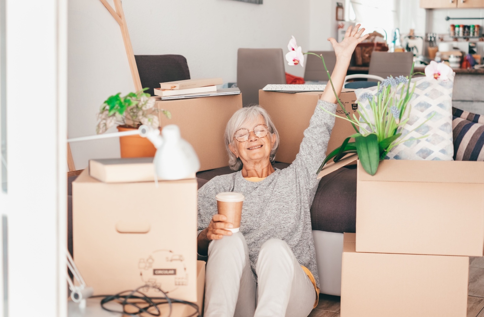 A senior celebrates with their arm in the air after finishing packing up their possessions into moving boxes.